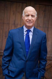 Photo fo Jim Falk in a suit and tie with a brown panel wall behind.